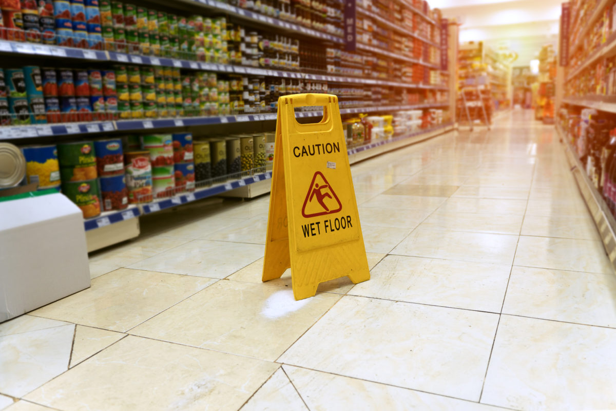 Wet floor sign on a supermarket floor against the background of blurry products standing on the shelves