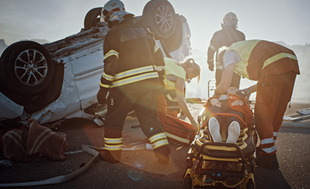 Image of firefighters at the scene of a vehicle rollover accident strapping the victim to a gurney.