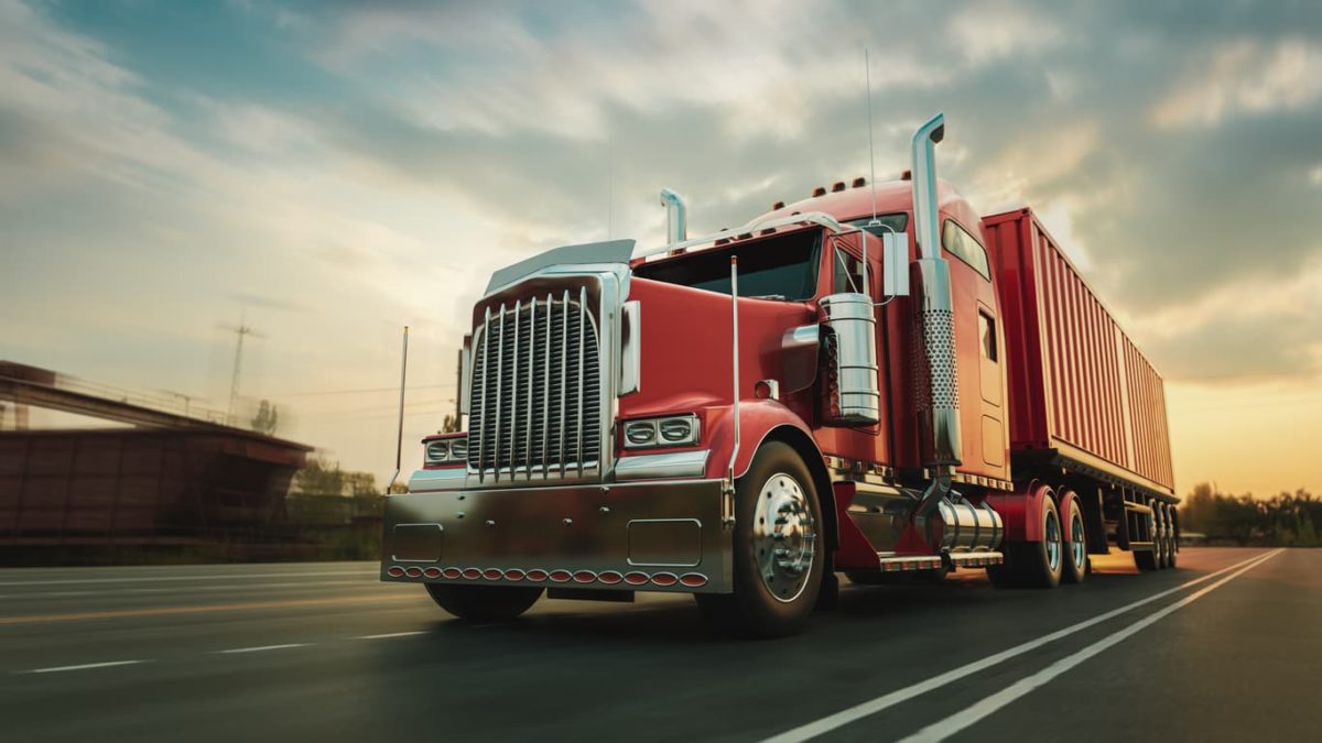 A red tractor-trailer coasts down the highway