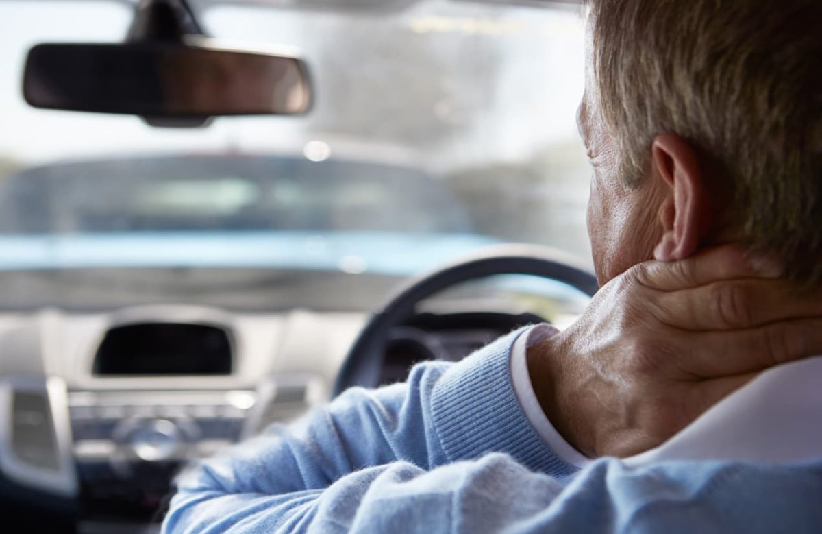 Male driver holding neck in pain while sitting in vehicle