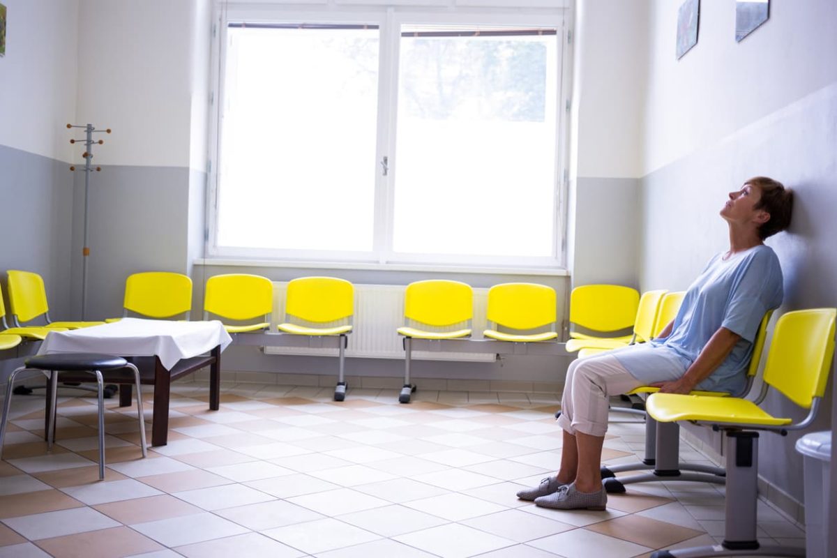 Woman sits in hospital waiting room with head tilted back in disbelief and anguish.